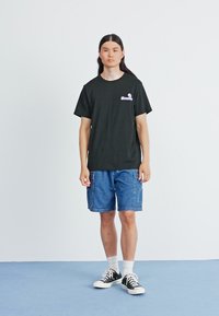 Tricou negru din bumbac cu logo violet, asortat cu pantaloni scurți din denim albastru cu buzunare laterale și teniși negri cu accente albe.