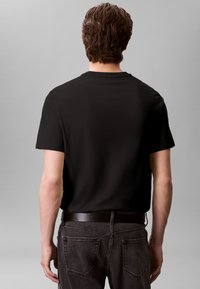 T-shirt preta de algodão com mangas curtas e decote redondo, usada com jeans cinza em ganga. O tecido tem uma textura suave, sem padrões visíveis.