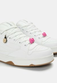 Vita sneakers med texturerat syntetiskt ovandel, rund tå, gummisulor, rosa snabblås och en liten kakcharm fäst vid snörningarna.