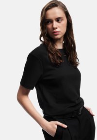 Sort bomulds t-shirt med korte ærmer, rund hals og afslappet pasform. Sammen med mørke bukser og et sort bælte. Glat tekstur.