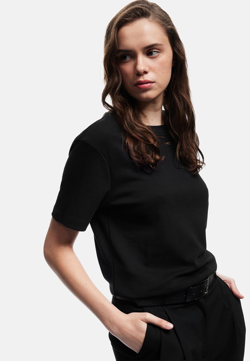 Sort bomulds t-shirt med korte ærmer, rund hals og afslappet pasform. Sammen med mørke bukser og et sort bælte. Glat tekstur.