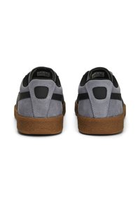 Paire de baskets en daim gris avec des bandes noires et des semelles marron texturées vues de dos sur fond blanc.