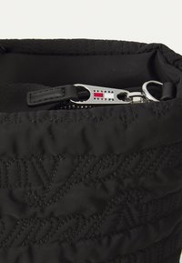 Black quilted nylon bag with embossed text, silver zipper hardware, and a logo tag featuring red, white, and blue accents.