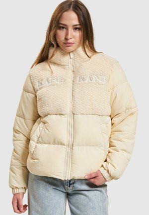 Padded jacket in light beige with a faux fur collar. Features embroidered "KANI," zip closure, and elastic cuffs. Textured and soft fabric.