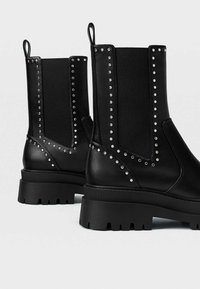 Bottines noires en cuir avec côtés élastiques, accents cloutés et semelle épaisse pour une meilleure adhérence et stabilité.