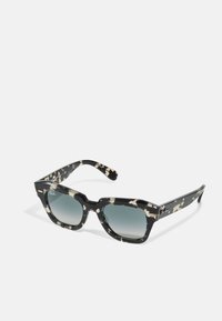 Melna un krēmīgi rakstainas saulesbrilles ar biezu rāmju, kvadrātveida formu un gradienta tonētu stiklu. Ray-Ban logo sānos.