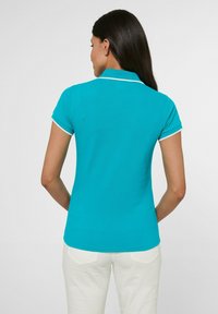 Turquoise poloshirt met korte mouwen, voorzien van witte rand rondom de kraag en de mouwen. Soepele textuur, aansluitend ontwerp. Achteraanzicht weergegeven.