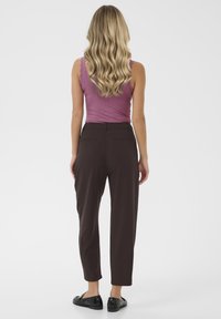 Light purple ribbed tank top paired with dark brown tapered trousers. The trousers have a smooth texture and two back pockets. Black slip-on shoes.