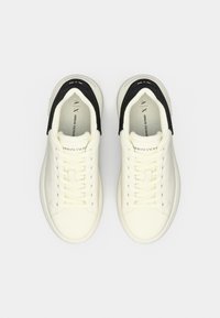 Ténis de couro branco com detalhes pretos, apresentando um design clássico com atacadores e material texturizado no calcanhar. Logo da marca visível no interior.