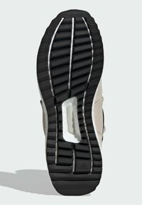 Suela de zapato de goma negra con ranuras profundas, sección intermedia blanca etiquetada "TORSION SYSTEM" y parte superior beige visible.