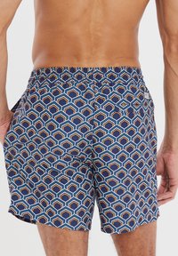 Costume da bagno con un motivo geometrico in blu navy, arancione e bianco. Vita elasticizzata, tasche laterali e materiale leggero.