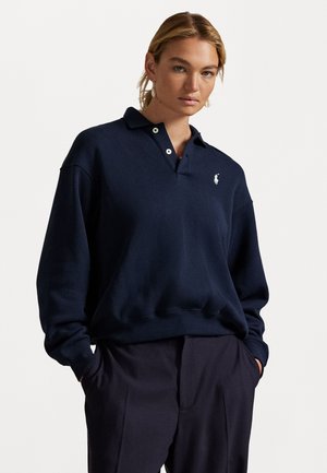 Marineblå genser med krage, to knapper, ribbede mansjetter og nederkant, samt liten hvit brodert logo på venstre bryst.