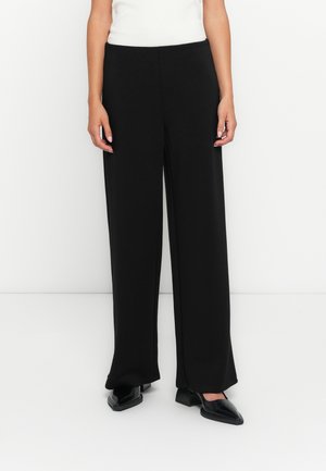 Schwarze weite Hosen mit glatter Textur, hoher Taille und taillierter Passform, kombiniert mit schwarzen Blockabsatzschuhen.