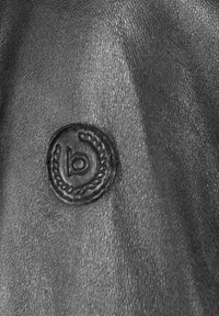 Crni teksturirani kožni materijal sa okruglim urezanim logom sa stiliziranim "b" i detaljem u obliku užeta.
