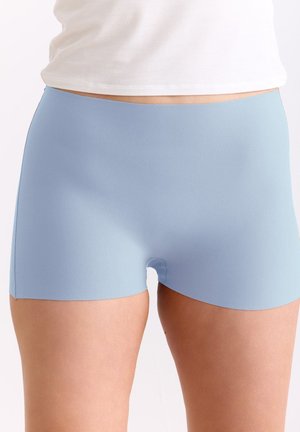 Hellblaue nahtlose Boyshort-Unterwäsche, die unter einem weißen Oberteil am unteren Rumpf und den oberen Oberschenkeln einer stehenden Person getragen wird.