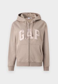 Beige zip-up hoodie made of soft fabric, featuring a large "GAP" logo in a lighter beige, with a front pocket and adjustable hood.