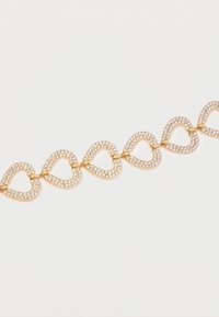 Guldtonet armbånd med en række sammenkoblede hjerteformer, hver prydet med glitrende klare rhinestones for en dekorativ effekt.