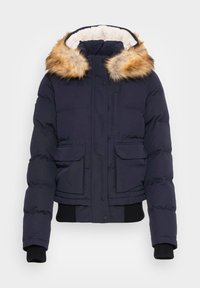 Veste rembourrée bleu marine avec garniture de capuche en fausse fourrure, dotée d'un col doublé en sherpa, de poches avant et de poignets et ourlet côtelés.