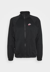 Zwarte full-zip Nike-jas met hoge kraag, lange mouwen, elastische manchetten en een rood-wit Nike-logo op de linkerkant van de borst.