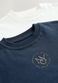 Dwie bluzy crewneck; jedna w kolorze granatowym z kremowym okrągłym logo, druga biała. Obie mają ribbowe dekolty i są uszyte z miękkiej bawełny.