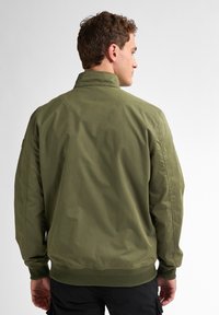 Jachetă bomber de culoare verde măslinie cu guler în picioare, manșete și tiv ribbate, textură netedă și detalii deloc vizibile ale cusăturii. Vizualizare din spate.
