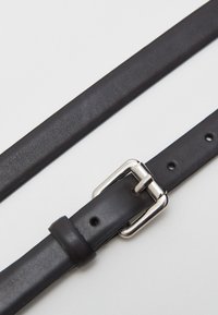 Schwarzer Leder Gürtel mit strukturiertem Finish, ausgestattet mit einer silbernen Metall-Schnalle und mehreren Löchern zur Größenanpassung.