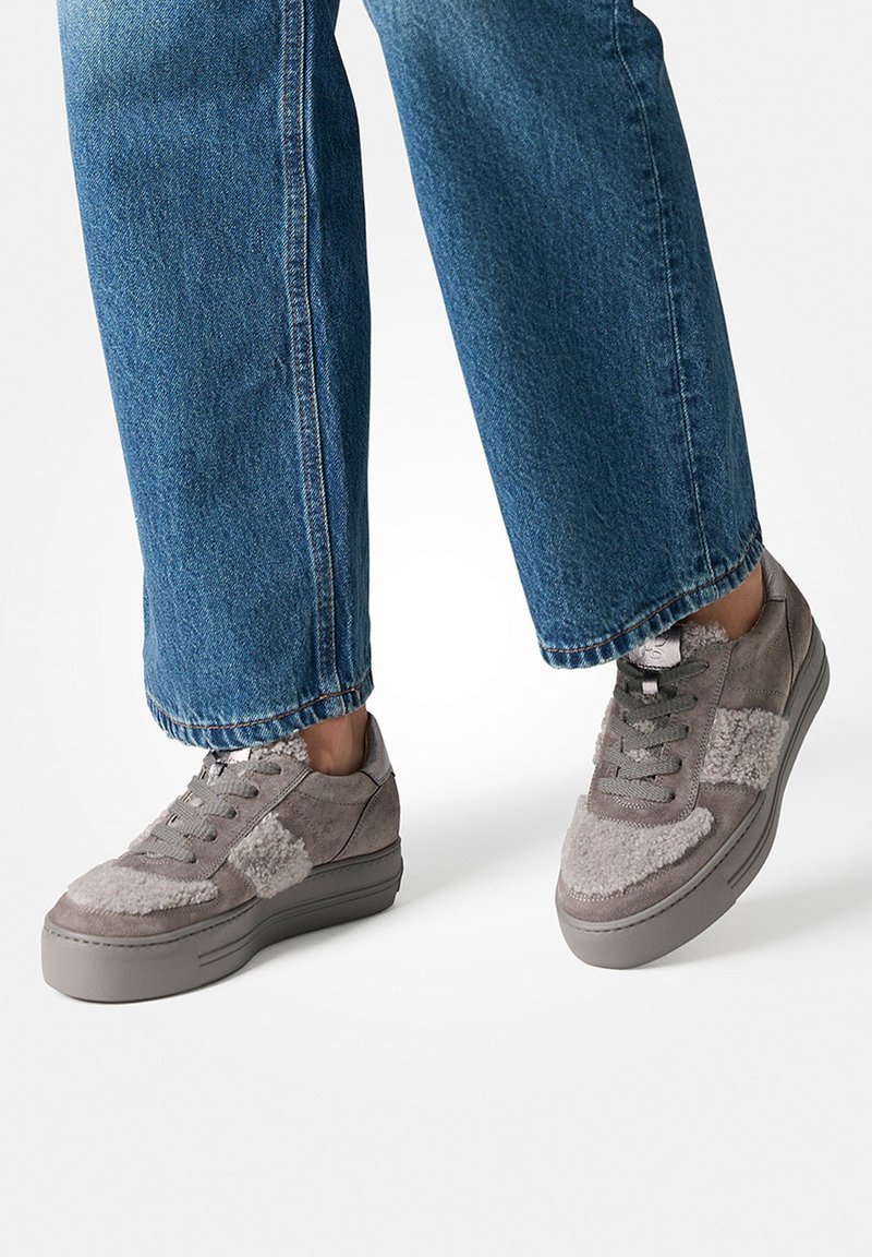 Szare zamszowe sneakersy z puszystymi akcentami, na platformie, z szarymi sznurowadłami. W połączeniu z podwiniętymi niebieskimi dżinsami.