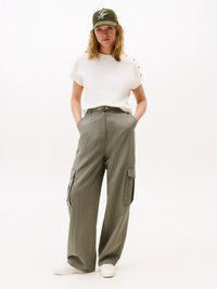White short-sleeve top with button accents, olive green wide-leg cargo pants, and white sneakers. Olive cap with embroidered logo.