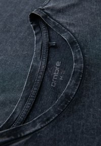 Tmavě modré tričko s kulatým výstřihem. Materiál má jemnou strukturu s vybledlým vzhledem. Známka značky "ombre" viditelná poblíž krku.