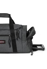 Grå tyg duffelväska med teleskophandtag, dragkedjor och svarta accenter. Har flera fack och en texturerad yta.