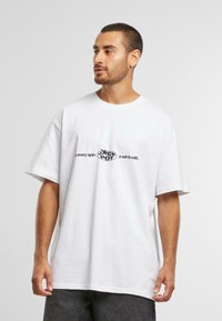 Hvit oversized T-skjorte laget av bomull, med en sentral trykt grafisk tekst i svart som leser: "Jackpot: Hver spinn er en vinn."