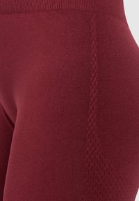 Bordeaux leggings met een gladde textuur en een gebreide tailleband, met een subtiel geometrisch patroon aan de zijkant.