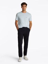 T-shirt de manga curta azul claro com um bolso no peito, combinado com calças escuras e ténis brancos, exibindo um estilo casual do dia a dia.