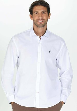 Chemise blanche à manches longues en coton, avec un petit logo noir sur la poitrine gauche et un col pointu.