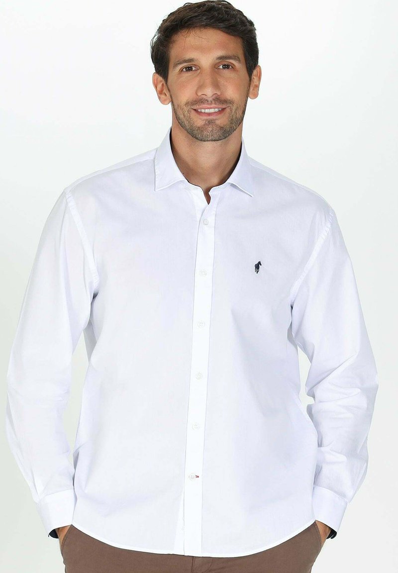 Chemise blanche à manches longues en coton, avec un petit logo noir sur la poitrine gauche et un col pointu.