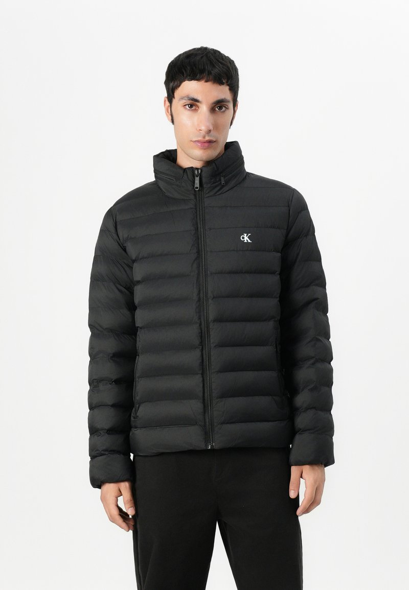 Must ümmarguste õmblustega jope kõrge krae ja esikäe tõmblukuga. Omab horisontaalset tepitud mustrit ja väikest logo rinnal.