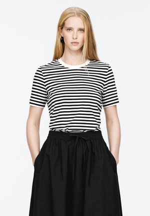 Kurzarm-T-Shirt mit schwarz-weißen Streifen und rundem Halsausschnitt, kombiniert mit einem schwarzen Rock mit elastischem Bund und seitlichen Taschen.