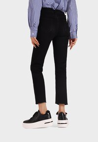 Jeans neri a vita alta con orlo sfrangiato, abbinati a sneakers platform nere con suola bianca e dettagli testurizzati.