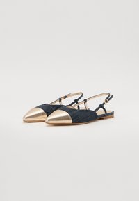 Ballerines slingback en denim avec un bout pointu en métal doré, présentant des sangles ajustables et une semelle en bois plat. La couleur est bleu foncé.