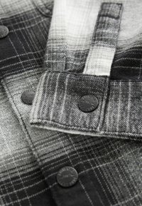 Close-up of black and white plaid fabric with black buttons labeled "Authentic 1982" on a folded cuff.