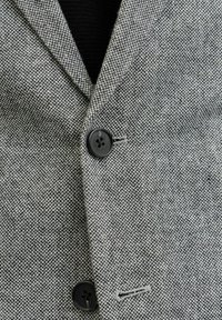 Blazer grigio a motivo houndstooth con tessuto texture, dotato di colletto a rever, due bottoni neri e dettagli con una sola fessura.