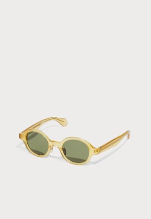 Yellow transparent sunglasses with oval green lenses. Features curved arms and subtle design accents on temples. Plastic material.