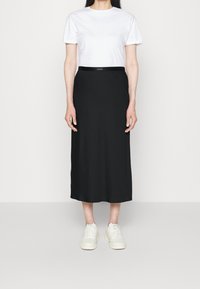 Jupe midi noire en tissu doux, avec une taille lisse. Associée à un t-shirt blanc uni et des baskets de couleur claire.