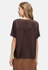 Blouse en satin marron à manches courtes avec un décolleté large et une coupe droite, présentée de dos. Coutures plates visibles le long des bords.