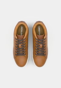 Bruine leren sneakers met een gladde textuur, donkerbruine veters en een witte rubberen zool. Merkwaarde "JACK & JONES" zichtbaar aan de binnenkant.
