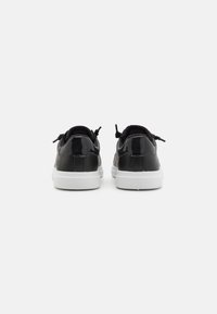 Sneaker in vernice nera con suola in gomma bianca, dotati di talloni testurizzati e lacci sottili per una calzata sicura.