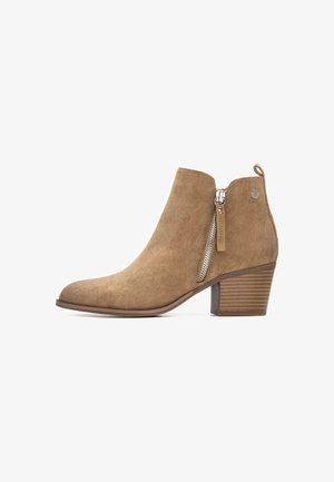Bota de tobillo de ante en tono beige con un tacón de bloque texturizado, detalle de cremallera asimétrica en el lateral y puntera redondeada.
