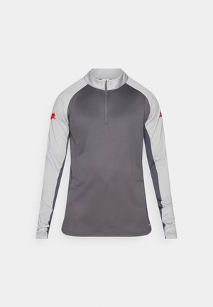 Camiseta deportiva de manga larga en gris con acentos grises. Cuenta con una cremallera de un cuarto en el cuello y un logo rojo en la manga izquierda. Textura de tela suave.