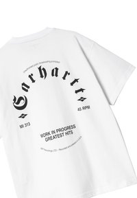 Camiseta blanca de algodón con texto gráfico y logo negro en la parte posterior. Mangas cortas y corte relajado. El diseño incluye texto circular y acentos.