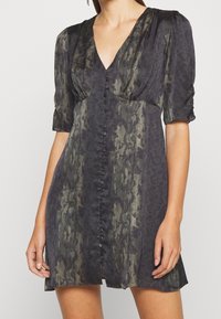 Short-sleeve dress in dark green and black with a textured animal print, deep V-neck, and front button closure, offering a flowing silhouette.